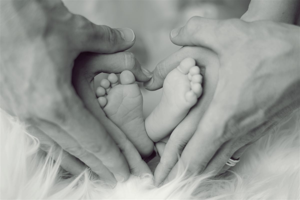 canva---grayscale-photo-of-baby-feet-with-father-and-mother-hands-in-heart-signs